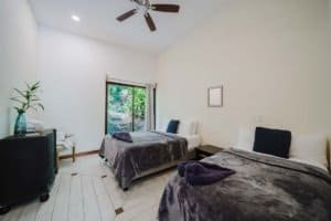 Furnished bedroom with two beds, balcony, and tropical view in Dominical.