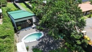 Aerial view of a modern home with a kidney-shaped pool, surrounded by lush trees and a green-roofed,.