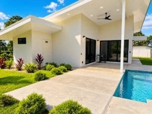 Dominical Real Estate modern house with pool and patio, white walls, lush lawn and clear blue sky.