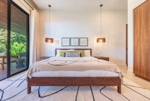Bedroom with king bed, wooden furniture, pendant lights and sliding glass door to balcony.