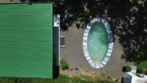 Aerial view of an oval pool near a green-roofed building and surrounding trees.