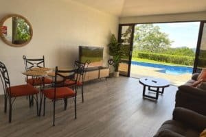 Panoramic poolside living room with dining set and large sliding glass doors.