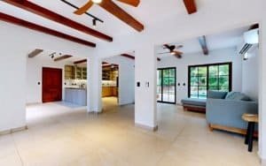 Spacious living area with exposed wooden beams, modern kitchen, and large windows in a tropical home.