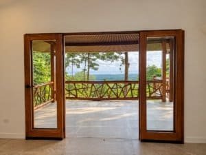 Dominical ocean view from covered deck with wood railing and framed glass doors.