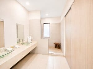 Bright bathroom with double glass sinks, beige tiles, and a small window.