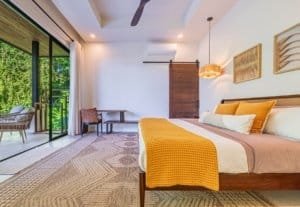 Luxurious bedroom with warm orange throw pillows and a sliding glass door to a tropical balcony.
