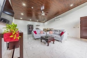 Bright living room with white marble flooring, gray sectional sofa, wood ceiling, and modern decor.