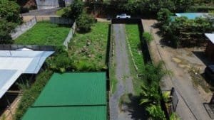 Aerial view of a real estate lot with a long driveway, green surroundings, and adjacent structures.
