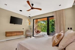 Luxuriously appointed bedroom with ceiling fan, hanging chair and sliding glass doors to greenery.