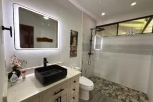 Modern bathroom with vessel sink, backlit mirror, glass shower, and patterned tile floor in Costa RI.