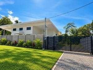 Modern single-story home with white exterior, gated driveway, and manicured lawn in Costa Rica.