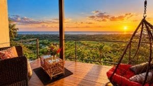 Panoramic sunset over jungle and ocean from a tropical terrace with seating and hanging chair in Dom.