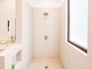 Bright walk-in shower with large window and beige tiles in Costa Rica condo.