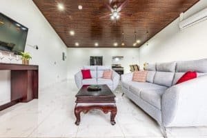 Bright living room with grey sofas, white marble floor, dark wooden ceiling, and ceiling fan.