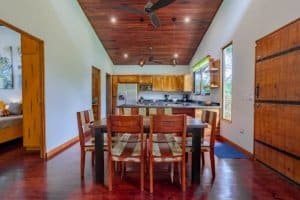 Turn-key Costa Rica home interior with wooden dining table and kitchen in background.