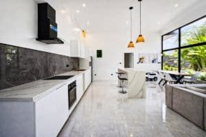 Open-concept kitchen and living room with stone countertops, modern fixtures, and large windows.