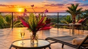 Ocean view terrace with tropical plants, sunset over the coast, lounge chairs and drinks.