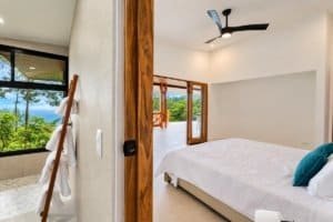 Ocean view bedroom with king bed, glass doors to balcony, and ceiling fan.