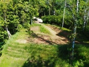 Elevated land parcel with grassy terraces, surrounding trees, and a dirt path through a forested lot.