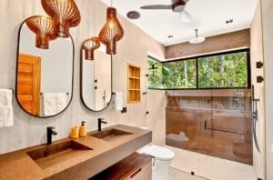 Luxurious jungle bathroom with double sinks, large window and glass shower.
