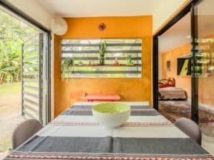 Interior view of a Costa Rican home with vibrant orange walls and lush greenery outside.