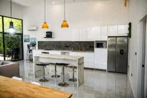 Bright modern kitchen with white cabinets, marble island, and stainless steel refrigerator.
