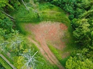 Aerial view of a cleared elevated plot surrounded by dense tropical trees.