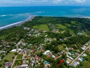 Aerial view of a coastal town with homes, greenery, and a nearby beach under blue skies.
