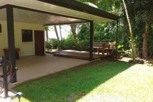 Covered patio with wooden deck, chair swing, and lush Costa Rican garden.