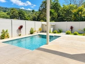 Modern pool with clear blue water, private fenced yard and lush hillside backdrop.
