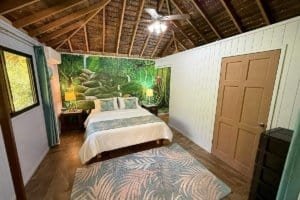 Bedroom with jungle mural, wooden ceiling, and natural light in Dominical.