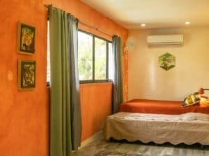 Interior of a bedroom with orange walls, large window, and two beds in Dominical.