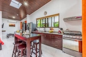 Spacious kitchen with island, dark cabinets, stainless steel stove and window view.