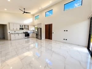 Bright kitchen and spacious living area with high ceilings and large glossy white tiles.