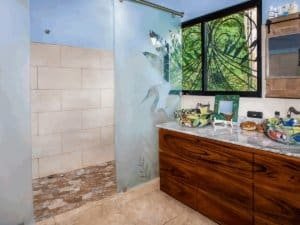 Bathroom with tropical rainforest view, wooden cabinet, and decorative items.