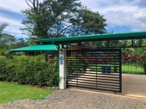 Turn-key coastal home entrance with green awning and black gate in tropical landscape.