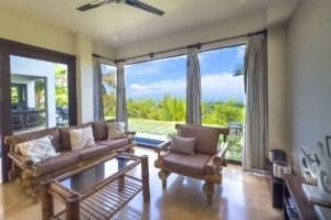 Spacious living room with ocean view, modern furniture, and tropical scenery.