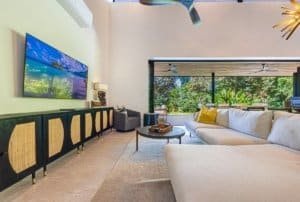 Bright living room with large glass doors opening to lush outdoor area and ocean view.