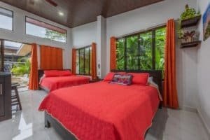Two red-themed bedrooms in Dominical Real Estate property with large windows.