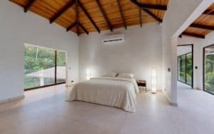 Spacious bedroom in a tropical home with high wooden ceiling, large windows, and private pool area.