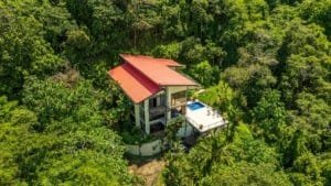 Panoramic hillside home with red roof among lush tropical forest near Dominical, with pool and deck.