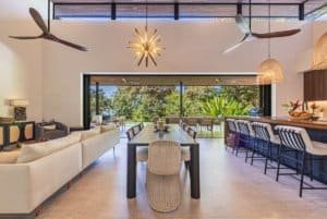 Bright open-plan living and dining area with panoramic outdoor seating and modern ceiling fans.