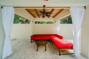 Outdoor lounge with red sofa, ceiling fan, and white curtains in Dominical.