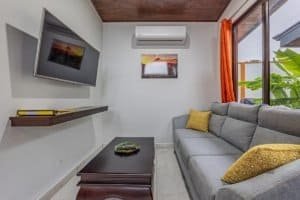 Cozy living room with gray sectional sofa, wall-mounted TV, and large window in Dominical Costa Rica.