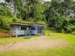 Small container home in lush green forest with outdoor seating and trampoline.