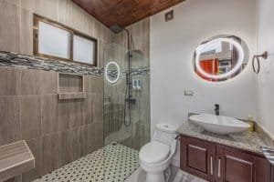 Modern bathroom with glass shower, round mirror, and granite vanity in Dominical.