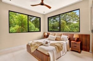 Luxurious bedroom with large windows overlooking lush greenery and pool area.