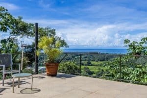 Panoramic ocean and valley view from terrace with seating and potted plants.