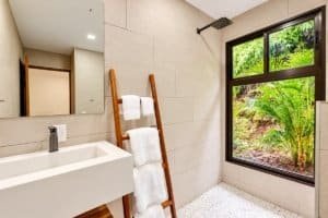 Ocean view bathroom featuring a modern sink, wooden ladder towel rack and lush tropical greenery.