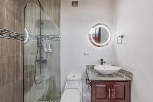 Modern bathroom featuring glass shower, circular mirror, and granite countertop.